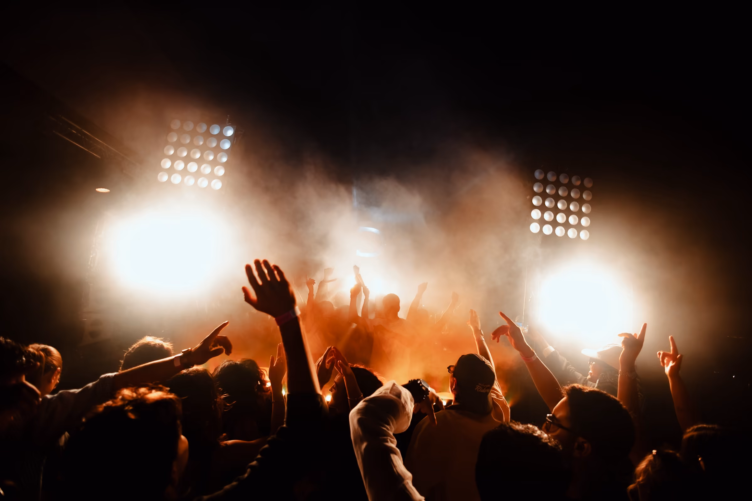 Hands in the air in front of two LED blinders burning through smoke