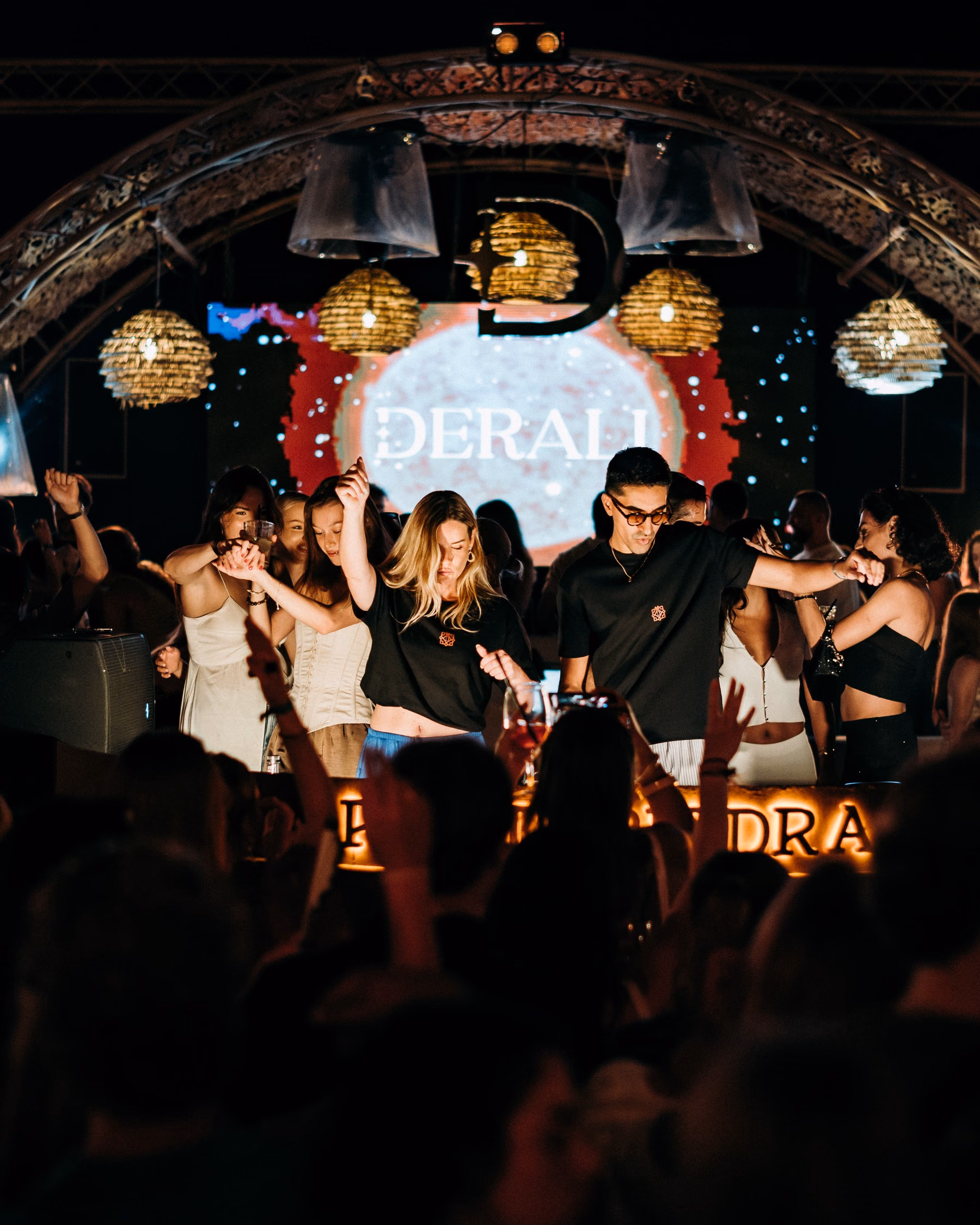 Lisa and Yassine at the booth beneath the lit Derali arch, dancers either side and the crowd filming