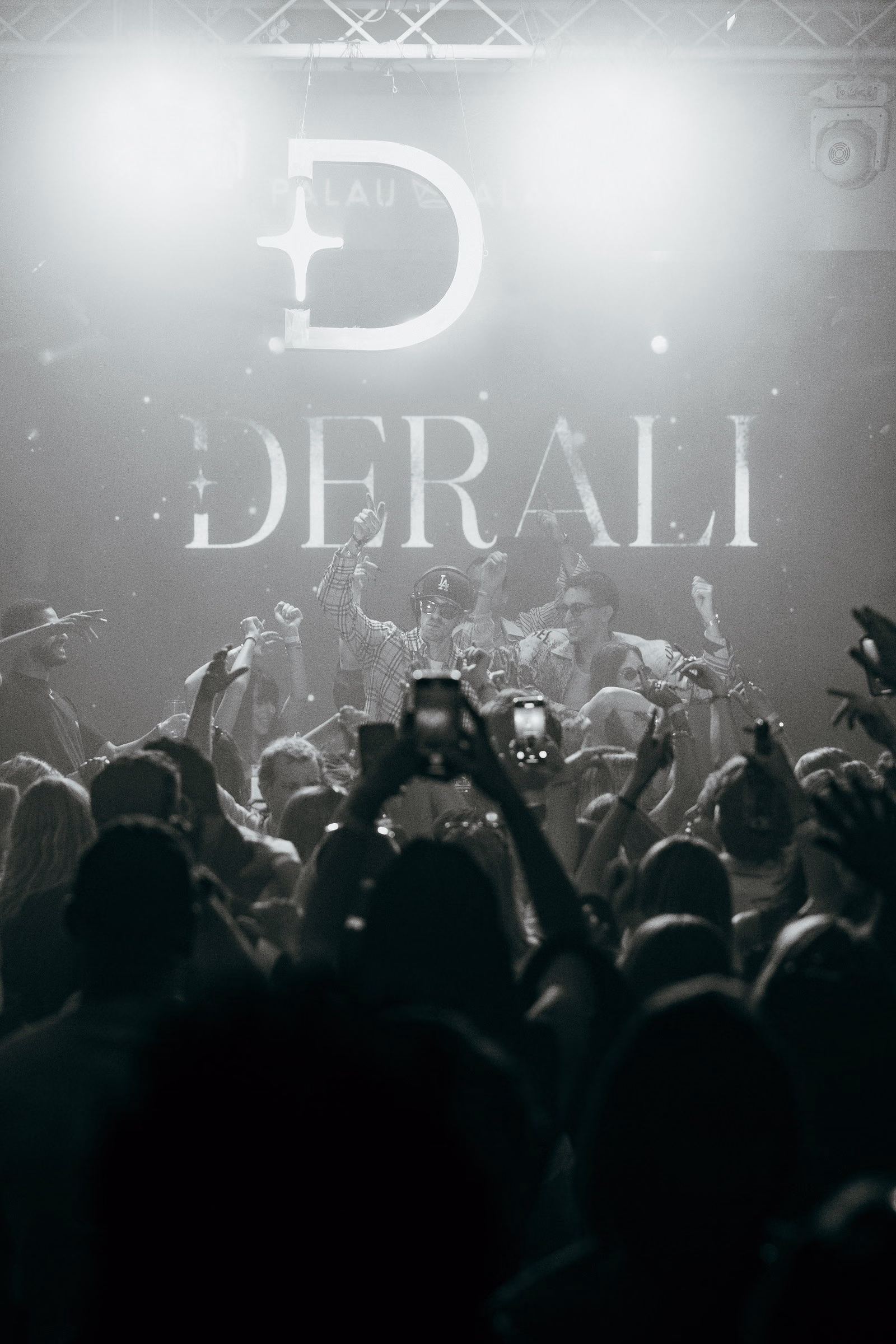 The Derali monogram and wordmark lit above the crowd at Palau Alameda, in black and white