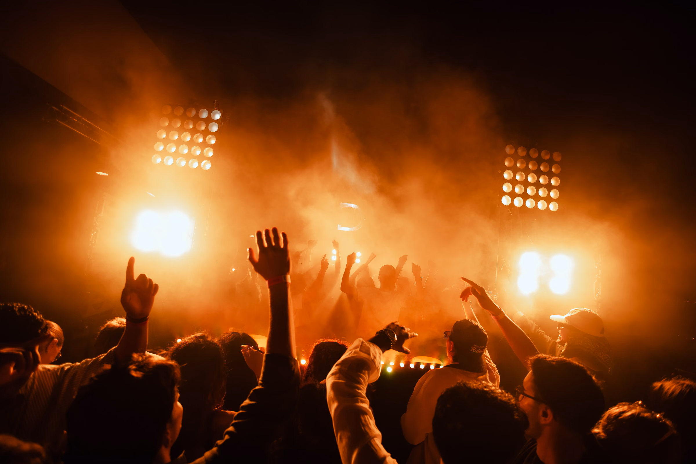 Blinders and orange haze over an open-air crowd with their arms up