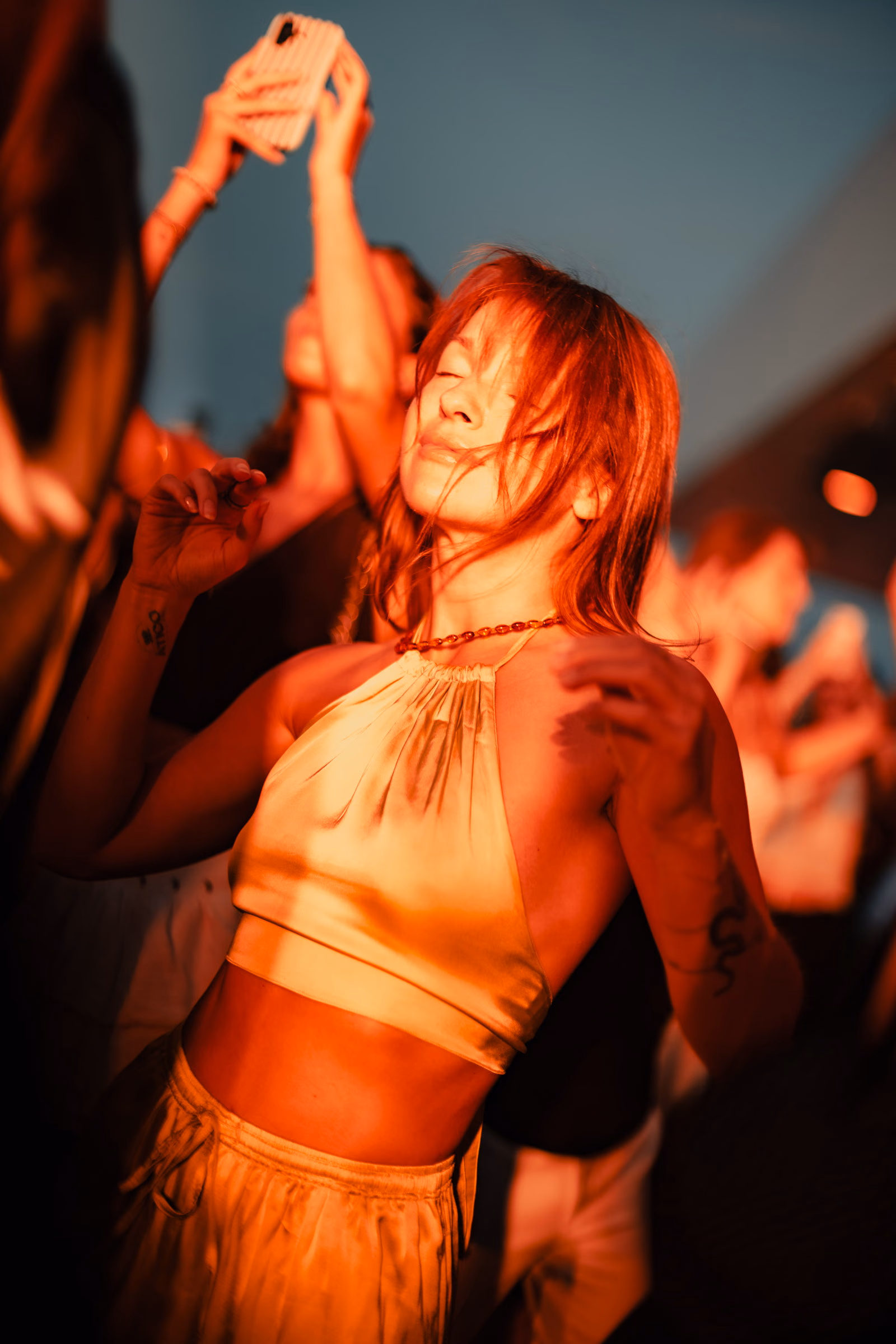 A woman dancing with her eyes closed in gold light, phones raised behind her