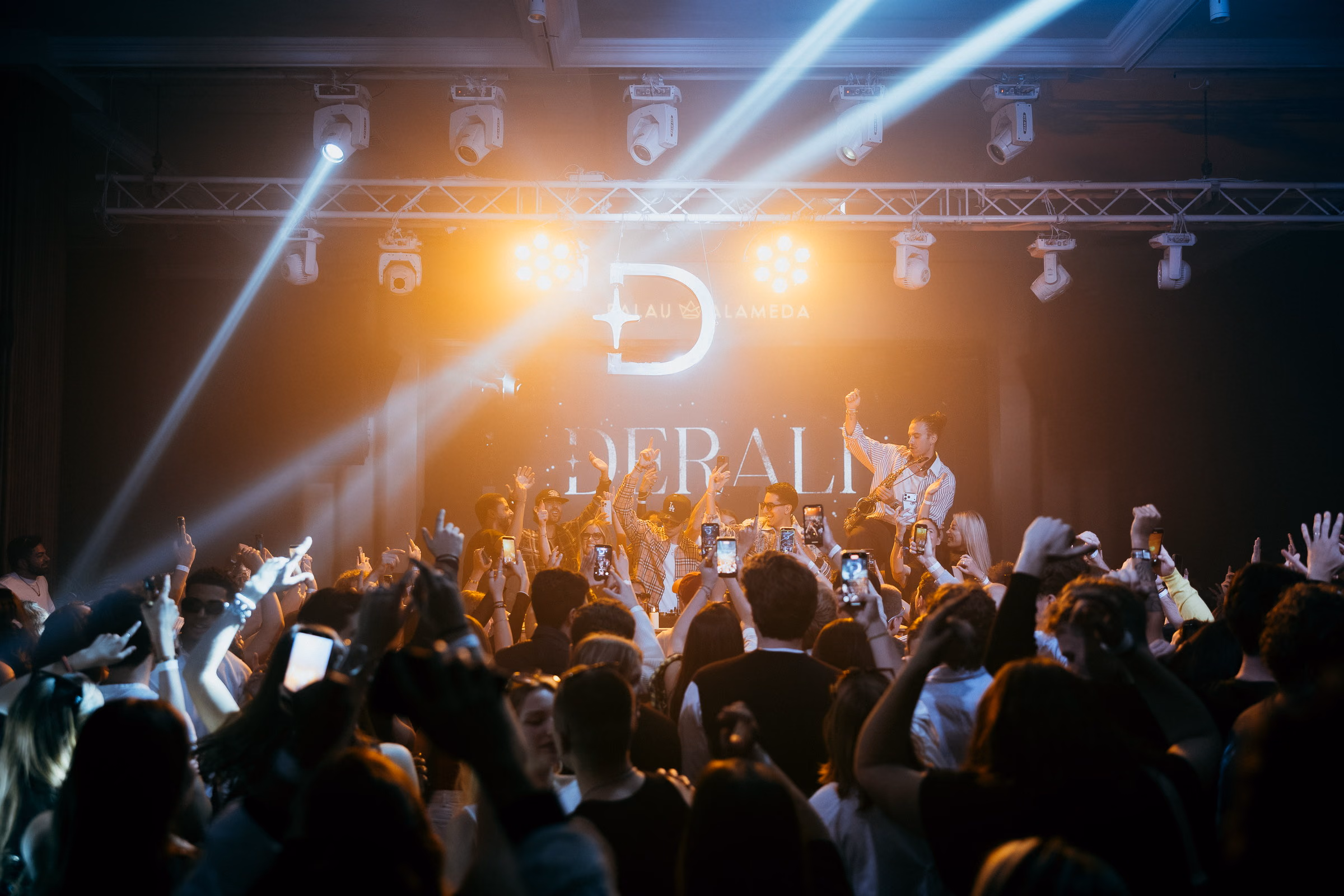 Amber beams crossing over the Derali wordmark at Palau Alameda, the crowd filming