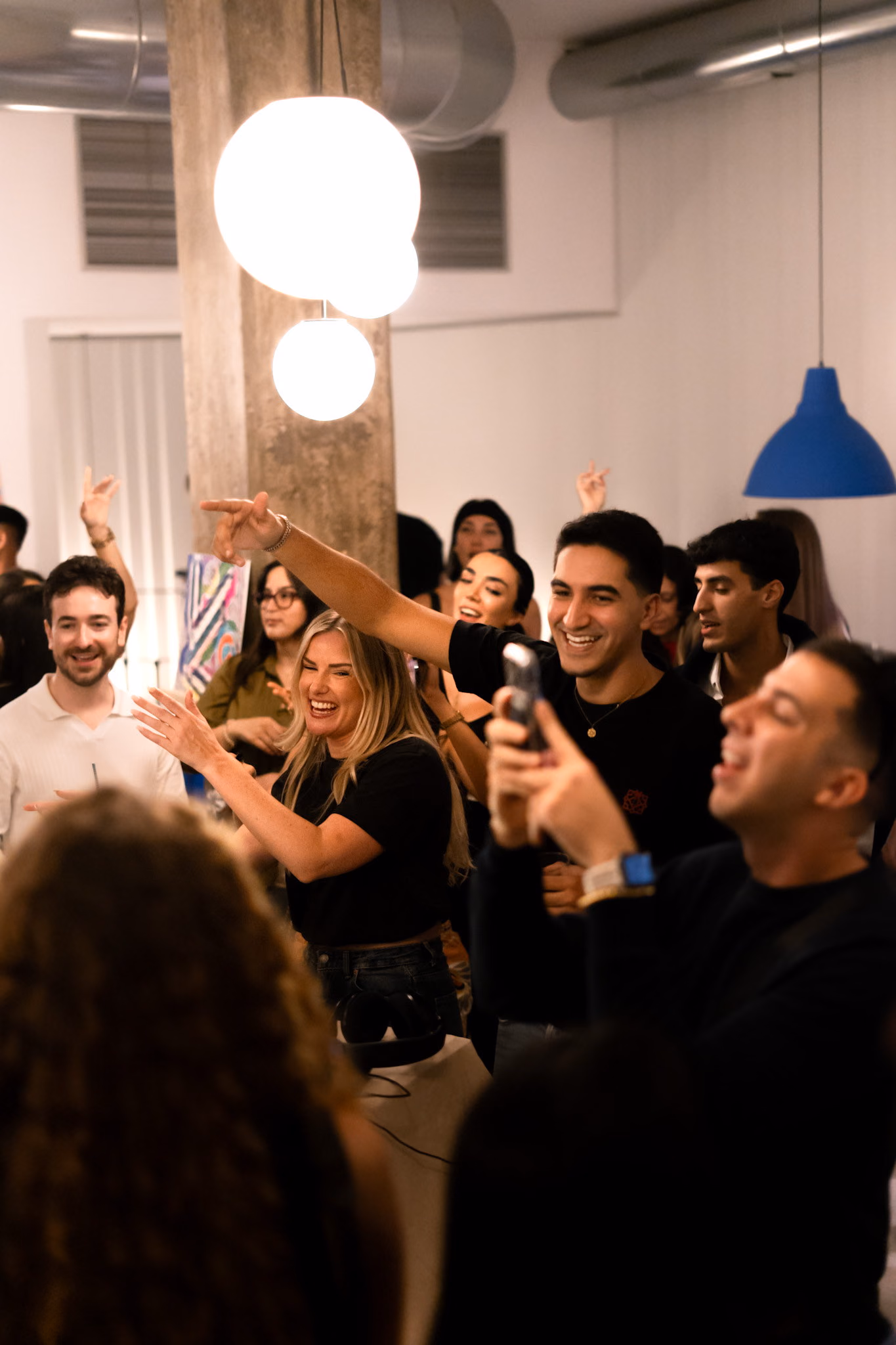 A group laughing and filming in a white space in daylight, globe lamps overhead
