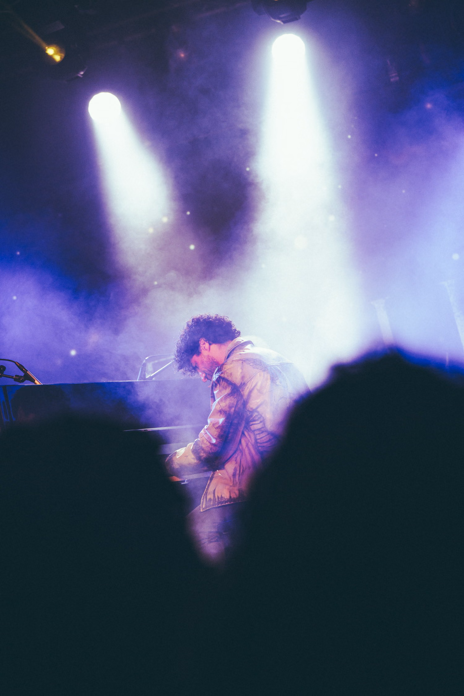 A pianist bent over the keys under violet beams and haze