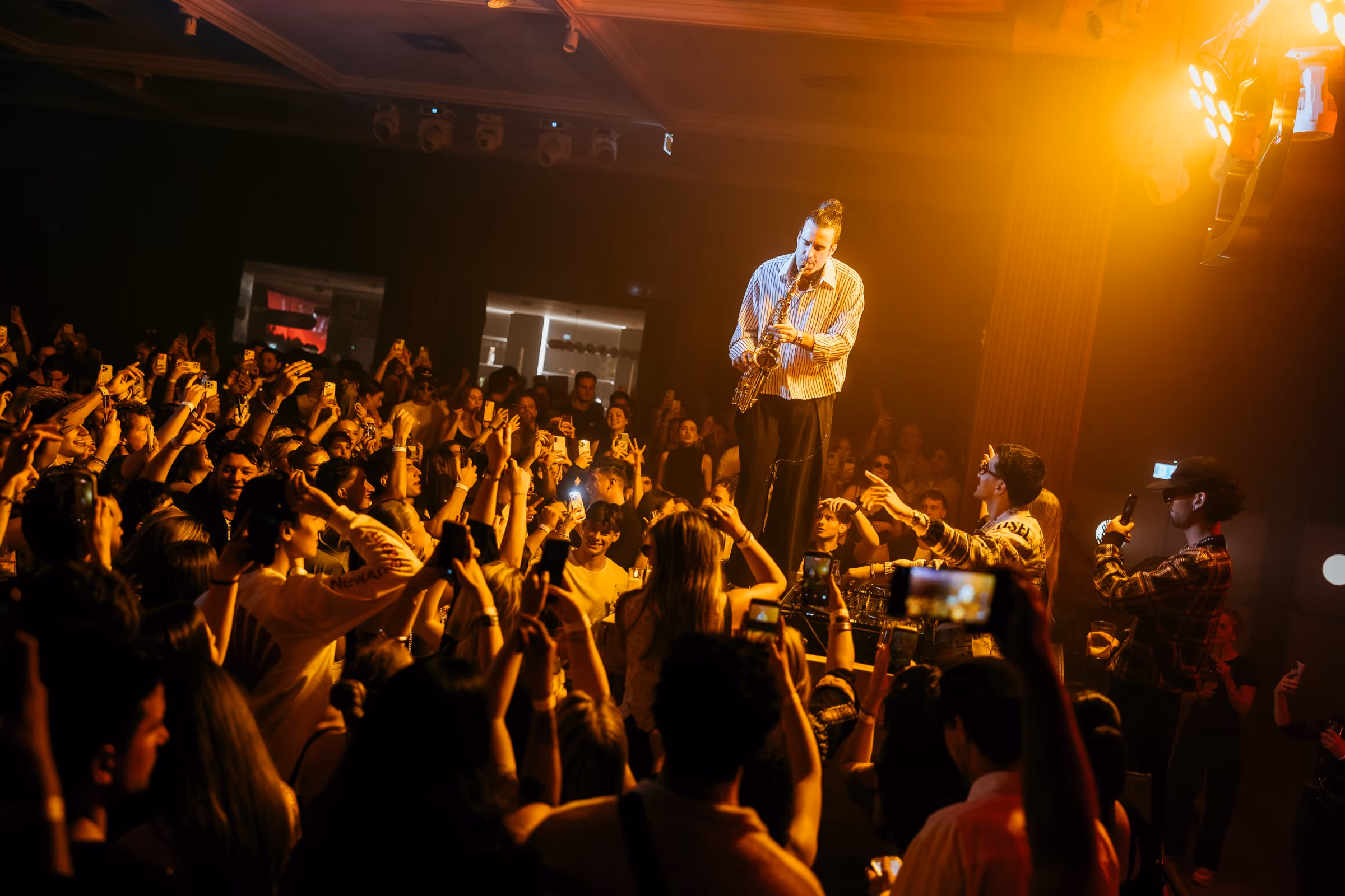 A saxophonist playing on stage above the crowd, lit gold