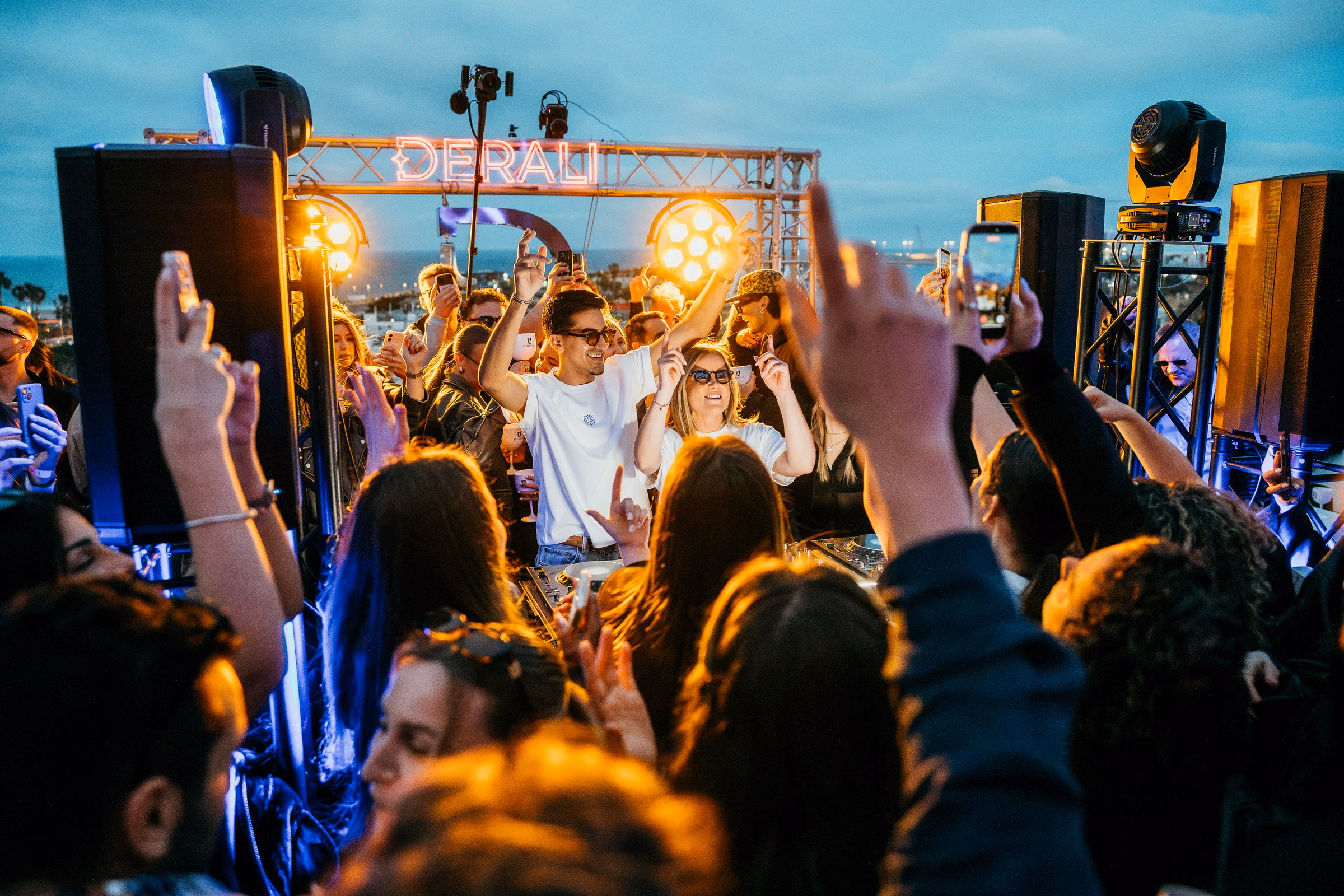 The Derali truss sign on the rooftop at Veles e Vents at dusk, the crowd beneath it